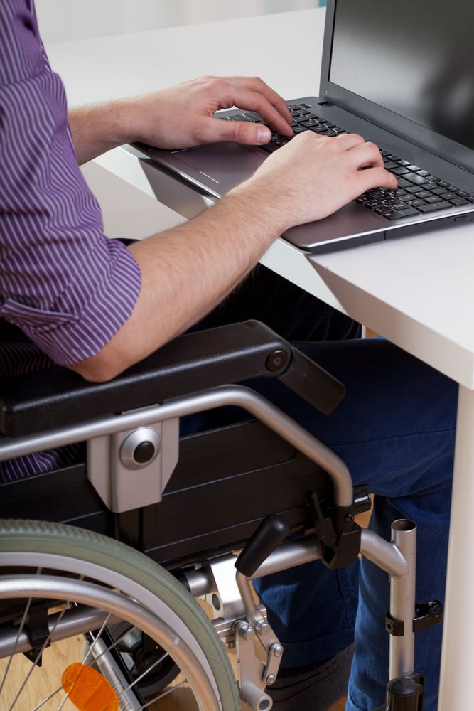 Man on wheelchair working on laptop, vertical Man on wheelchair working on laptop, vertical